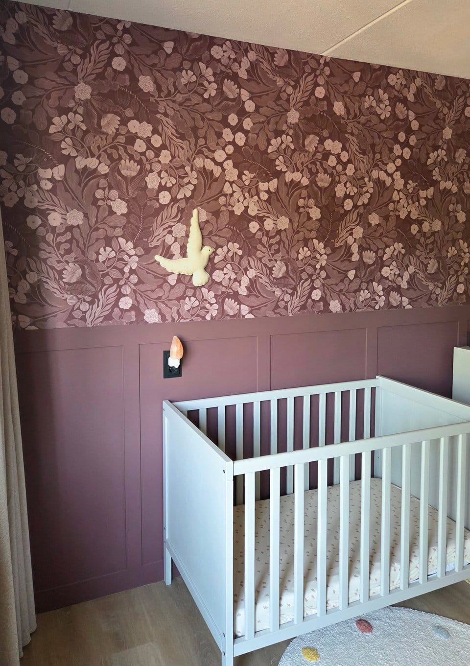 Mauve bloemenbehang boven de lambrisering in de babykamer
